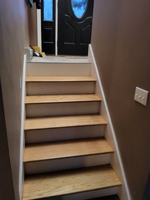 Finished indoor staircase with light oak treads, white painted risers and side trim, leading up to a landing and a black front door with an oval glass panel