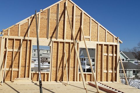 Wood-framed gable wall with two large window openings, temporary diagonal bracing and a blue sky behind